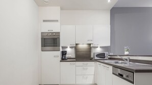 A modern kitchen with white cabinets, a built-in oven, a microwave, and a coffee maker. - Apartment With Modern Kitchen (Blankenberge)