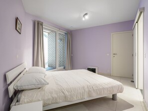 A bedroom with a bed, a nightstand, a window with curtains, a door, and a ceiling light. - Apartment With Modern Kitchen (Blankenberge)