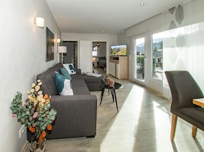 A modern living room with a grey sectional sofa, a small round table, and a TV in the background. - Holiday Home Zugspitze (Fuessen)