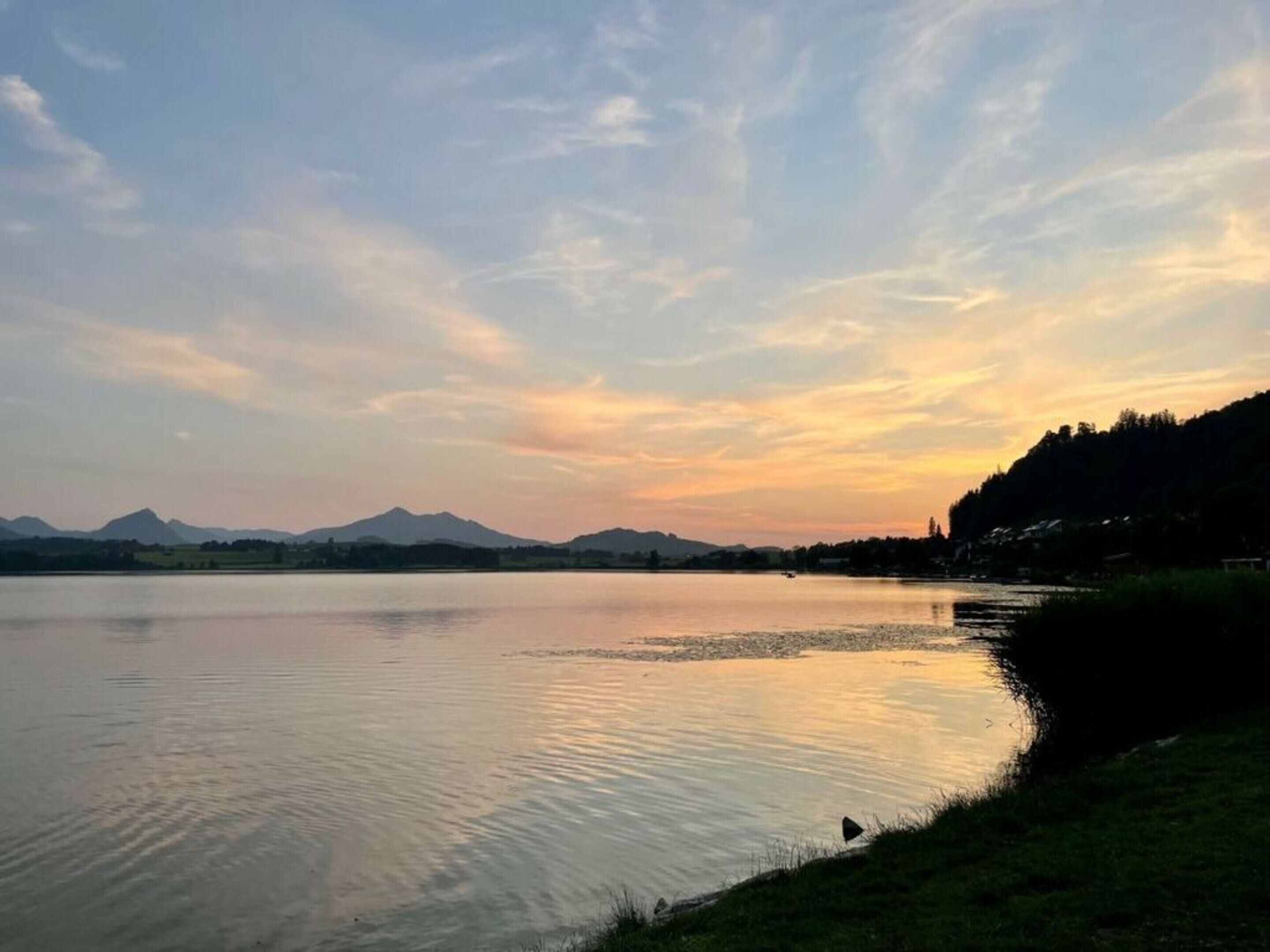 A calm lake with mountains in the background and a clear sky.