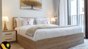 A neatly made bed with a wooden headboard, two bedside lamps, and a wall-mounted picture of a tree. - Vogue | Breeze Creek Beach | Waterfront Living (Dubai)