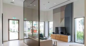 A modern hotel room with a large TV, a sofa, a small table, and a glass partition.