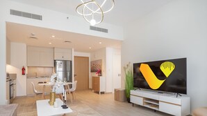 A modern living room with a flat-screen TV, a dining area with a table and chairs, and a kitchen with a refrigerator and stove. - Vogue | Breeze Creek Beach | Waterfront Living (Dubai)