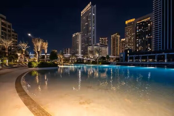 A nighttime view of a swimming pool with surrounding high-rise buildings and palm trees.
