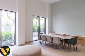 A modern dining area with a round table and chairs, large windows, and a view of greenery outside.