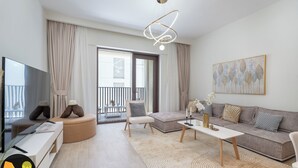 A modern living room with a television, sofa, coffee table, and a balcony with curtains. - Vogue | Breeze Creek Beach | Waterfront Living (Dubai)