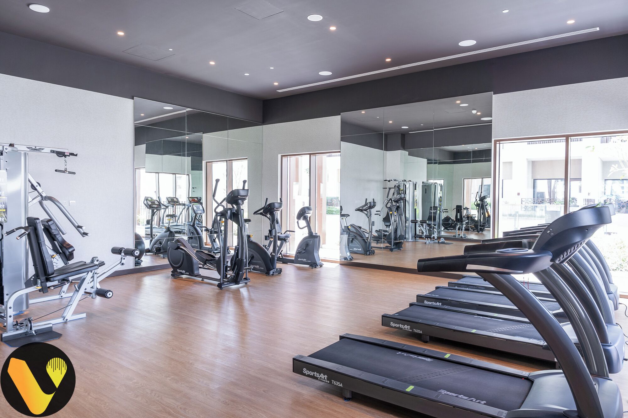 A modern gym with multiple exercise machines, including treadmills and weight equipment, and large mirrors on the walls.