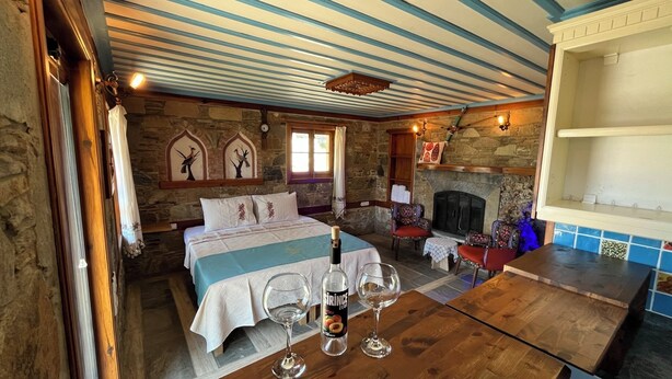 A cozy room with a bed, a fireplace, a table with wine glasses, and stone walls. - Çirkince Konak Şirince (Selçuk)