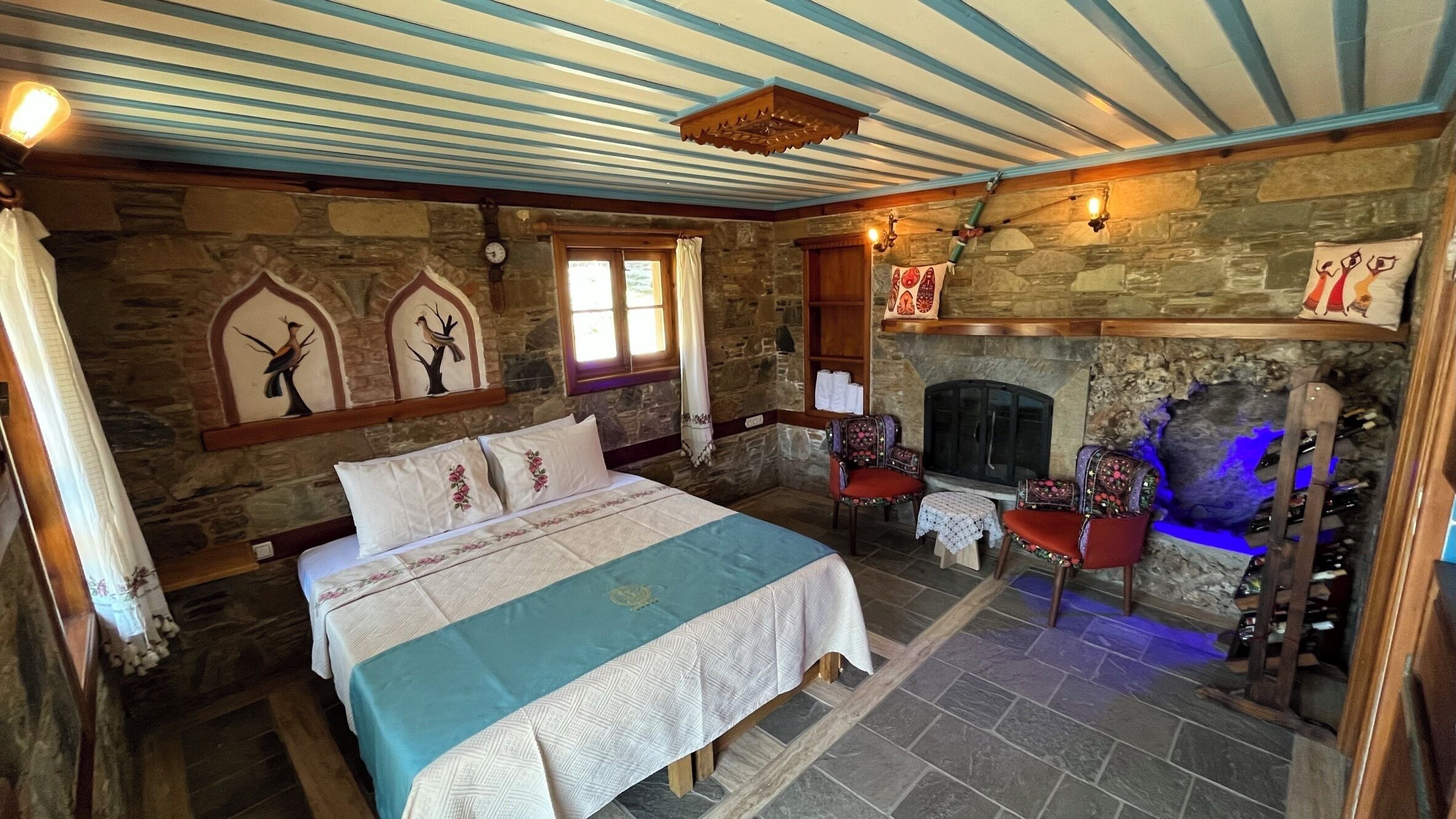 Un dormitorio con paredes de piedra, una cama, dos sillones, una chimenea y un banco de piedra.