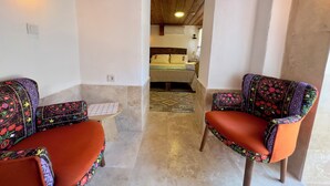 A narrow hallway leading to a bedroom with a bed, a nightstand, and a lamp. There are two chairs with colorful upholstery on either side of the hallway. - Çirkince Konak Şirince (Selçuk)