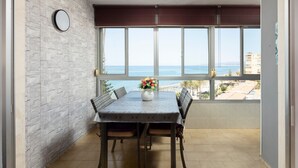 Un balcón con mesa, sillas, un jarrón de flores y vistas al mar.