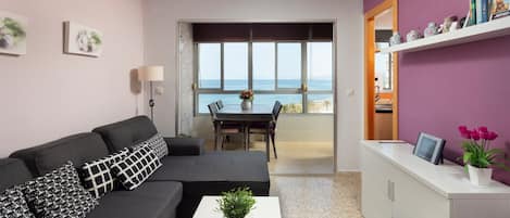 A modern living room with a sofa, coffee table, and a view of the sea through large windows.