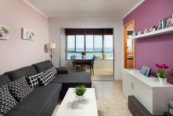 A modern living room with a sofa, coffee table, and a view of the sea through large windows.