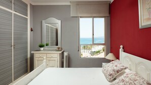 Un dormitorio con cama, cómoda, espejo, ventana con vistas y pared roja.