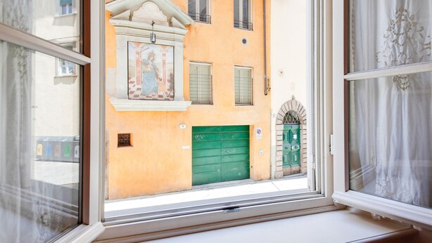 A window with a view of a building with a green door and a mural above it. - Mansion in Lucca Near Via Fillungo (Lucca)