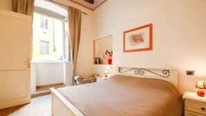 A bedroom with a bed, bedside table, lamp, and a window with curtains. - Mansion in Lucca Near Via Fillungo (Lucca)