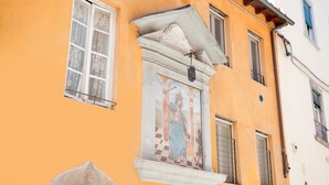 A building with a mural of a religious figure, a window with a decorative frame, and a small balcony. - Mansion in Lucca Near Via Fillungo (Lucca)