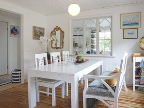 Un comedor con una mesa blanca, sillas y una ventana con vistas a una casa y árboles.
