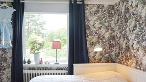 A bedroom with a bed, a window with curtains, a radiator, a lamp, and a floral wallpaper. - 4 Star Holiday Home in Brastad (Brastad)