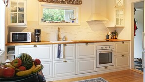 A kitchen with white cabinetry, a microwave, a stove, and a window with a view of greenery. - 4 Star Holiday Home in Brastad (Brastad)