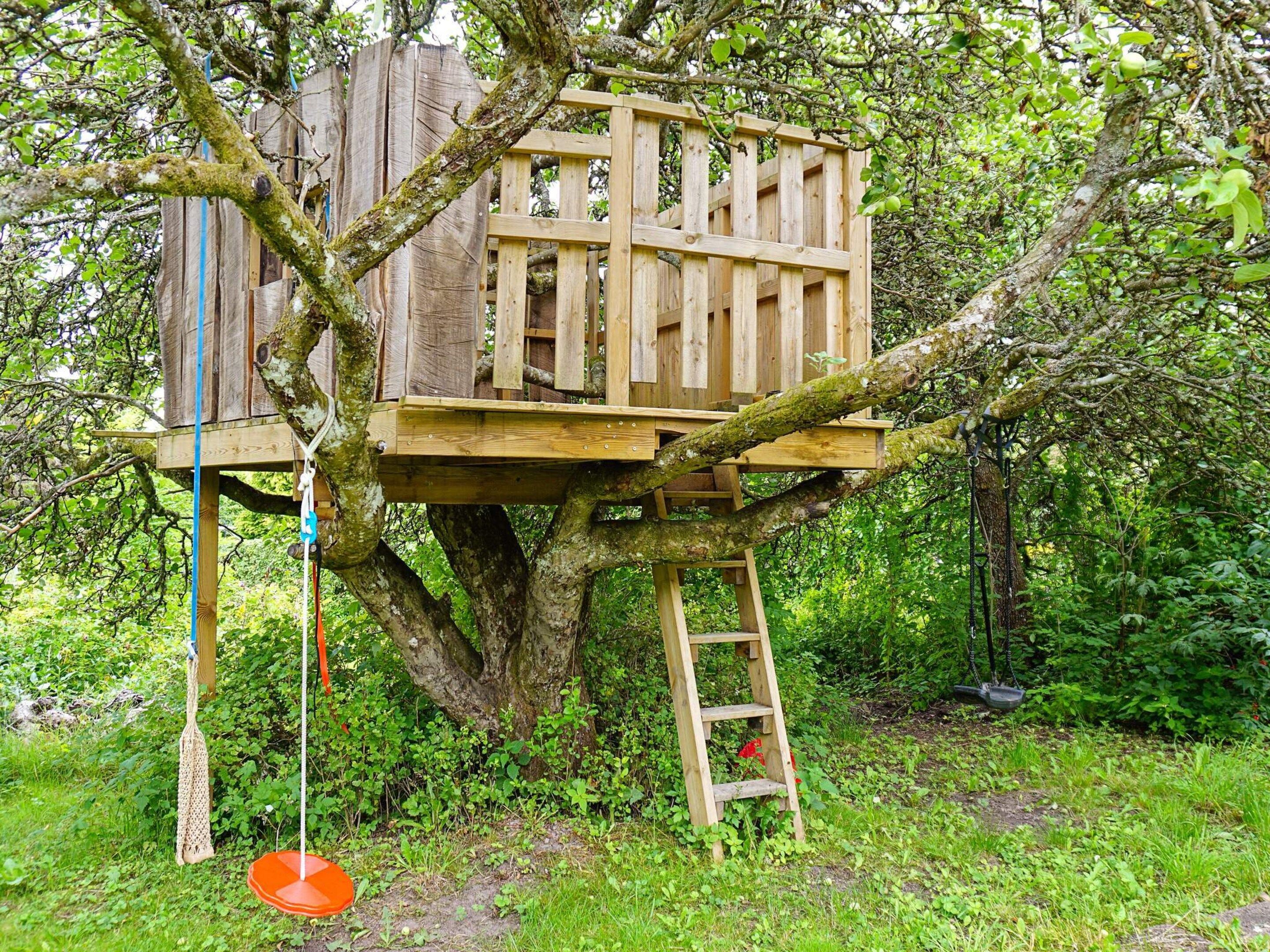 Una casa en el árbol de madera construida sobre un árbol grande, con una escalera y un columpio de cuerda.