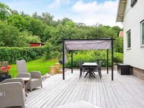 A wooden deck with outdoor furniture, a pergola, and a view of a lush garden and house. - 4 Star Holiday Home in Brastad (Brastad)