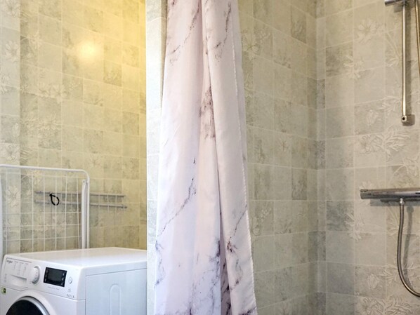 A bathroom with a washing machine, a shower with a marble curtain, and tiled walls. - 4 Star Holiday Home in Brastad (Brastad)