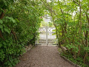 Un sendero conduce a una entrada con puerta y está rodeado de abundante vegetación.