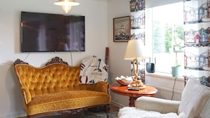 A living room with a large flat-screen TV, a vintage sofa, a lamp, and a window with patterned curtains. - 4 Star Holiday Home in Brastad (Brastad)