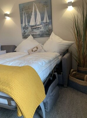 Una cama con un edredón amarillo, almohadas blancas y un cuadro de veleros en la pared.