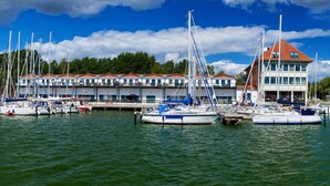 A marina with multiple sailboats docked, a building with a red roof, and a clear blue sky with clouds. - Holiday Apartment Harbor Flair (Karlshagen)