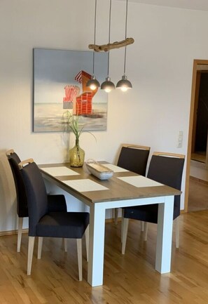 Un comedor con una mesa de madera, sillas negras y un cuadro de una playa.