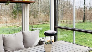 Habitación con ventana que da a un espacio cubierto de césped, un banco acolchado y una pequeña mesa con un florero.