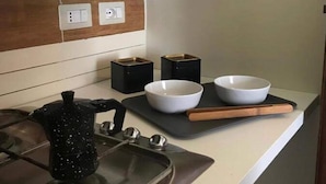 A modern kitchen with a stove, two bowls on a tray, a kettle, and two black containers. - Cozy Apartment in Torrenova (Capri Leone)