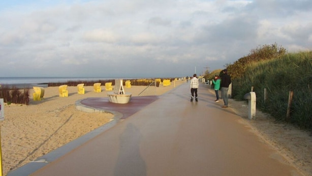 A paved walkway along a beach with yellow bollards and a boat sculpture. - Stefanie and Bernd Heumann (Cuxhaven)