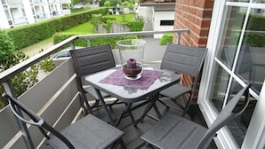 A balcony with a table and chairs, a glass vase with flowers, and a view of a green garden and buildings. - Stefanie and Bernd Heumann (Cuxhaven)