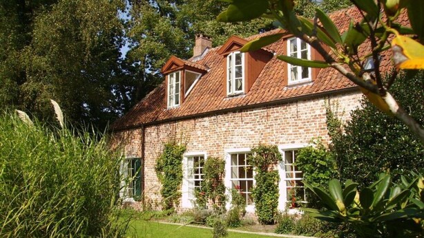 A stone house with a sloped roof, multiple windows, and a well-maintained garden with a gravel path. - Orangery Berum Modern Retreat (Hage)