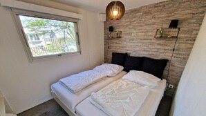 Un dormitorio con dos camas, una ventana, un estante empotrado con objetos decorativos y una pared con textura.