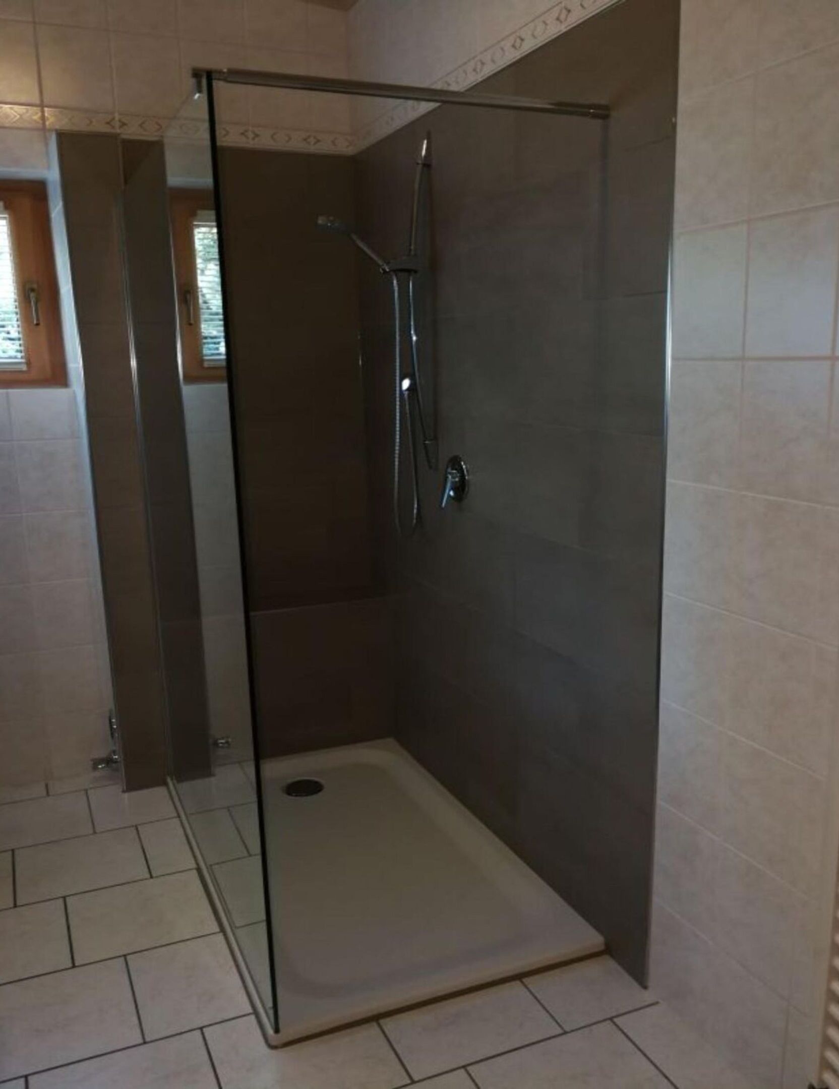 Une cabine de douche fermée par des parois en verre, avec un sol et des murs carrelés, une douchette à main et un robinet fixé au mur.