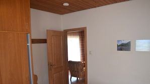 Ein Schlafzimmer mit einem Holfischschrank, einem Bett mit weißer Bettwäsche, einem Holzstuhl und zwei gerahmten Bildern an der Wand.