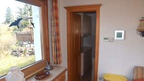Eine kompakte Küche mit Holdekor-Schränken, einem Fenster mit Gartenblick, einer kleinen Essecke mit gelbem Tisch und einer Holztür, die in einen anderen Raum führt.