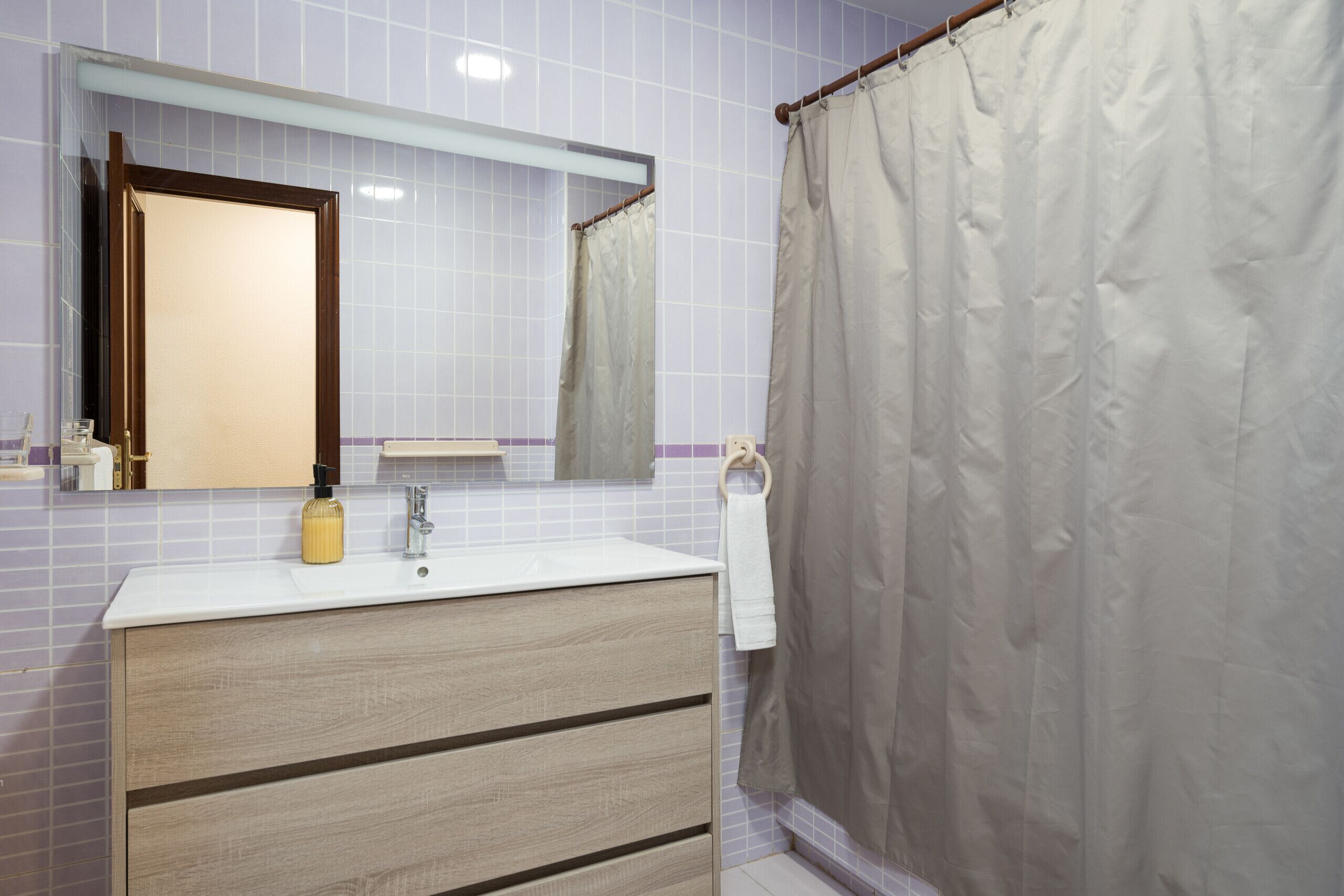 Un baño con tocador de madera, un espejo, toallero y cortina de ducha.