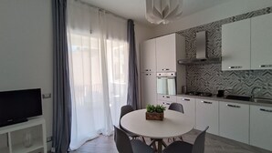 A modern kitchen with white cabinets, a built-in oven, and a gas stove. There is a dining table with chairs and a small plant on it.