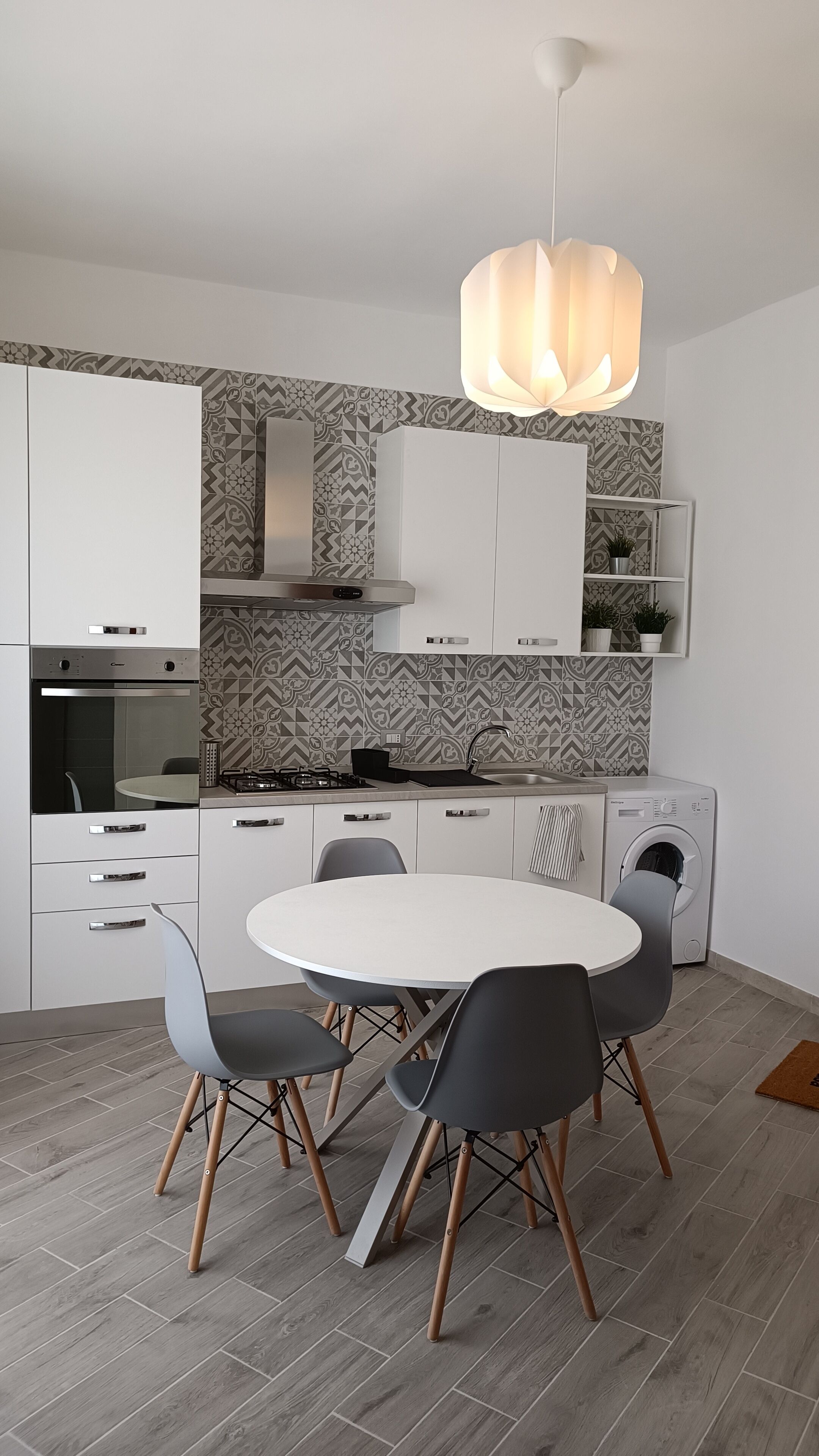 Een moderne keuken met witte kastjes, een ronde eettafel en grijze stoelen.
