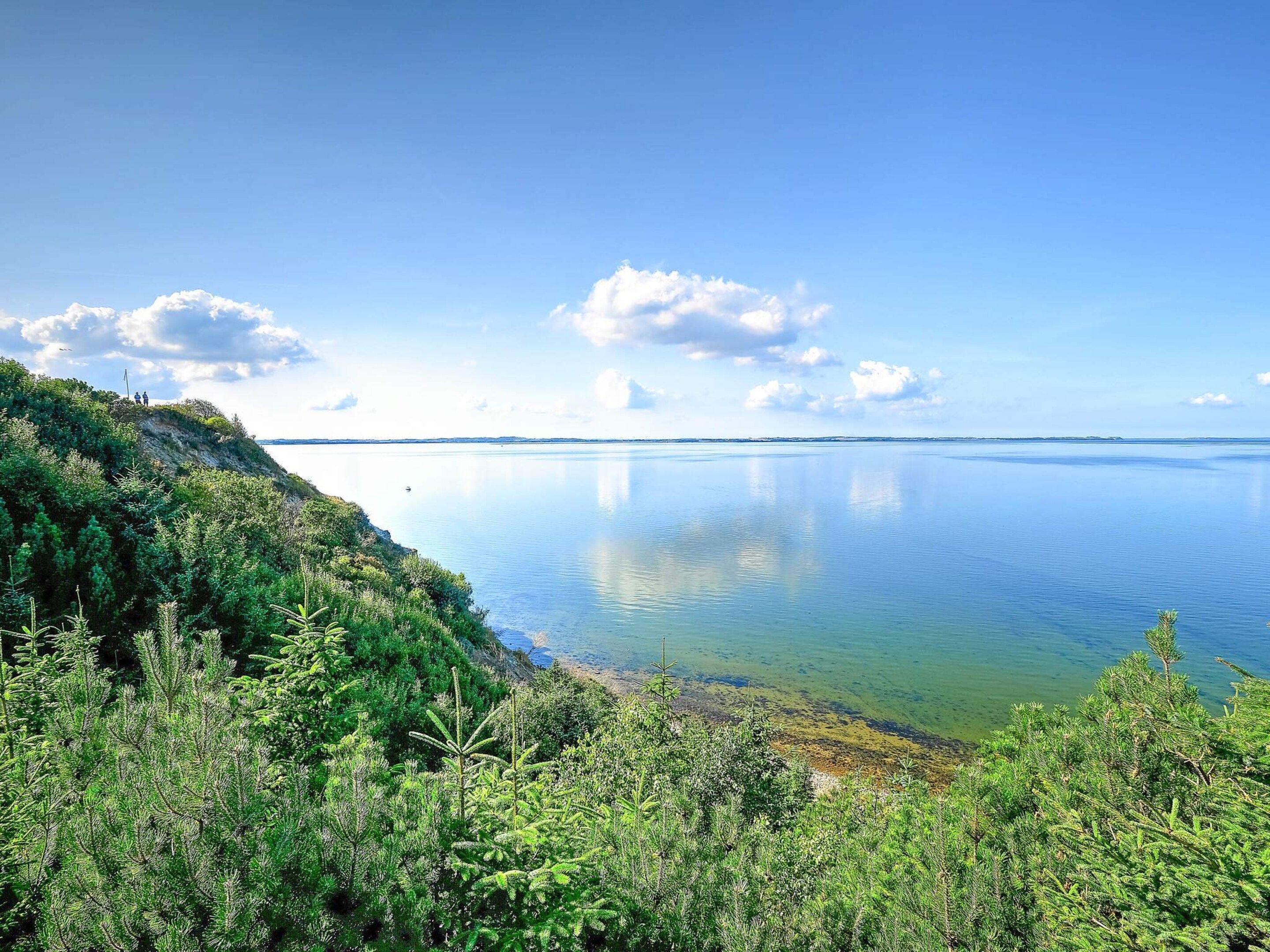 A coastal landscape with a clear view of the sea, a grassy hill, and a distant shoreline.