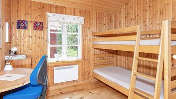 A room with wooden walls, a bunk bed, a desk with a chair, a window with a view of greenery, and a radiator.