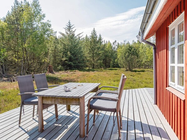 A wooden deck with a table and chairs, surrounded by a forested area. - 6 Person Holiday Home in Fur (Fur)