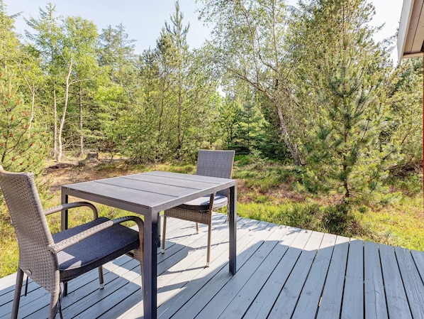 A deck with a table and two chairs, surrounded by trees. - 6 Person Holiday Home in Fur (Fur)