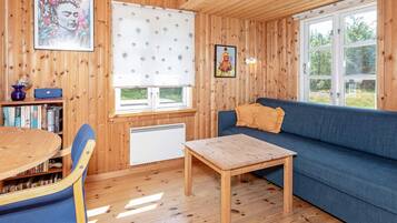 A cozy cabin interior with a wooden interior, a blue sofa, a dining table with chairs, and a bookshelf.