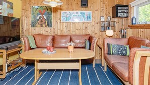 Um quarto aconchegante com teto de madeira, um sofá de couro marrom, uma mesa de jantar de madeira e uma televisão.
